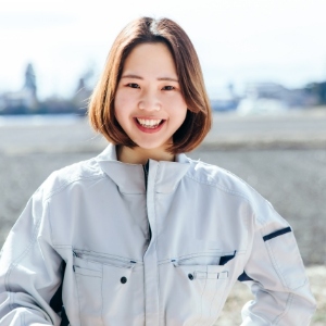 田んぼを背景に、作業着姿の女性が正面を向いて笑っている様子