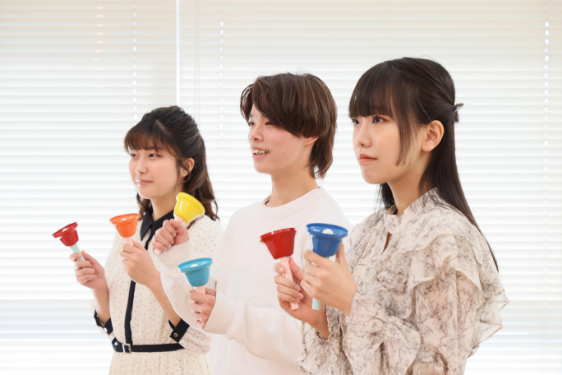 子ども学科の3人の男女学生がハンドベルを持っている様子