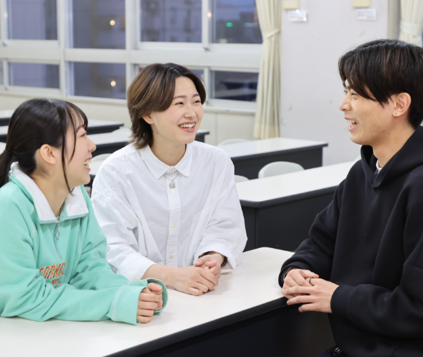 3人の男女学生が教室の中で談笑している様子